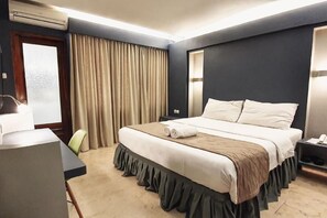 Habitació d'hotel amb un llit, una taula de treball, una cadira, una tauleta de nit i una finestra amb cortines.