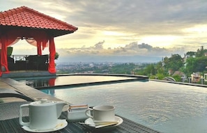 Zona de piscina con un pabellón de techo rojo, una mesa con tetera y taza, y vistas a un paisaje urbano.