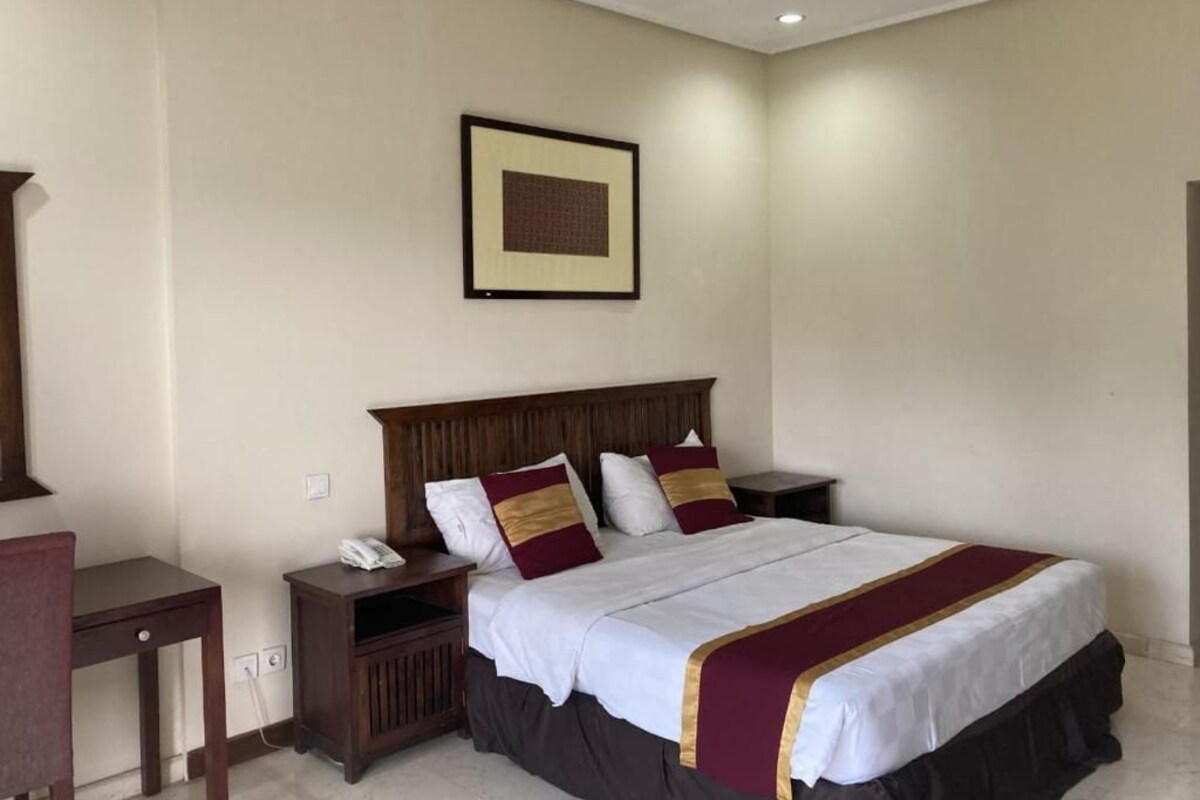 A hotel room with a large bed, a wooden headboard, a bedside table with a phone, and a framed picture on the wall.