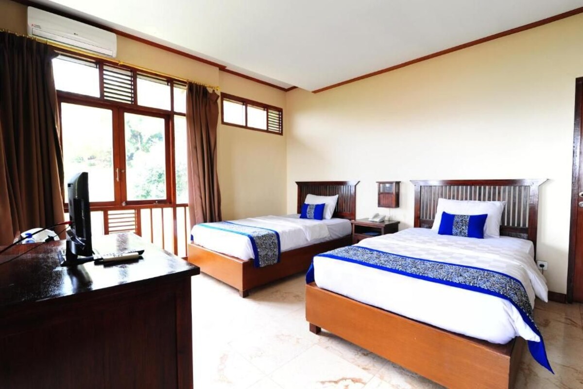 A hotel room with two beds, a desk with a computer, and a window with curtains.
