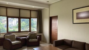 A room with a large window, a sofa, two armchairs, and a wooden coffee table. - Dago Highland Resort (Bandung)