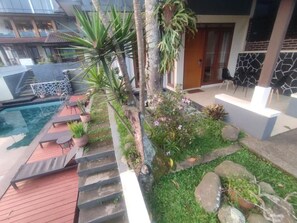 Zona de piscina con terraza de madera, sillones de descanso y un pequeño jardín con rocas y plantas.