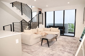 Un salon moderne avec un canapé, une table basse et un escalier doté de rampes noires.