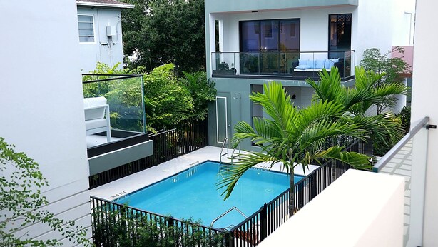 A modern residential building with a rooftop swimming pool, surrounded by greenery and a balcony with white outdoor furniture. - Luxury 1.65M 4-Story Townhome 3bed/3bath in the Heart of Brickell (Miami)