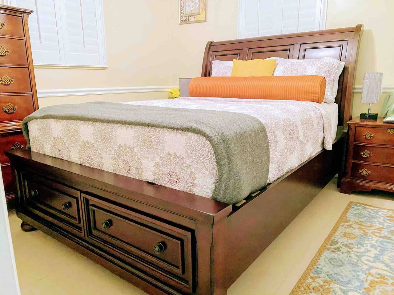 Een slaapkamer met een houten bed, een nachtkastje, een dressoir en een kamerkleed met dessin.