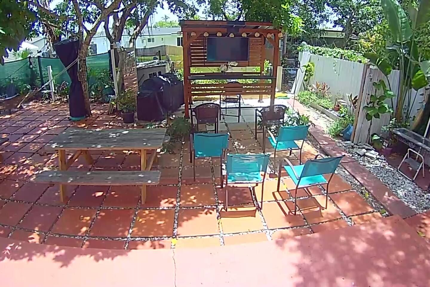 An outdoor patio with a wooden pergola, a barbecue grill, and several chairs and tables.