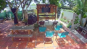 Um pátio externo com pérgola de madeira, churrasqueira e vários cadeiras e mesas.