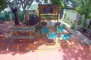 Terrassa exterior amb una pèrgola de fusta, un barbacoa i diverses cadires i taules.