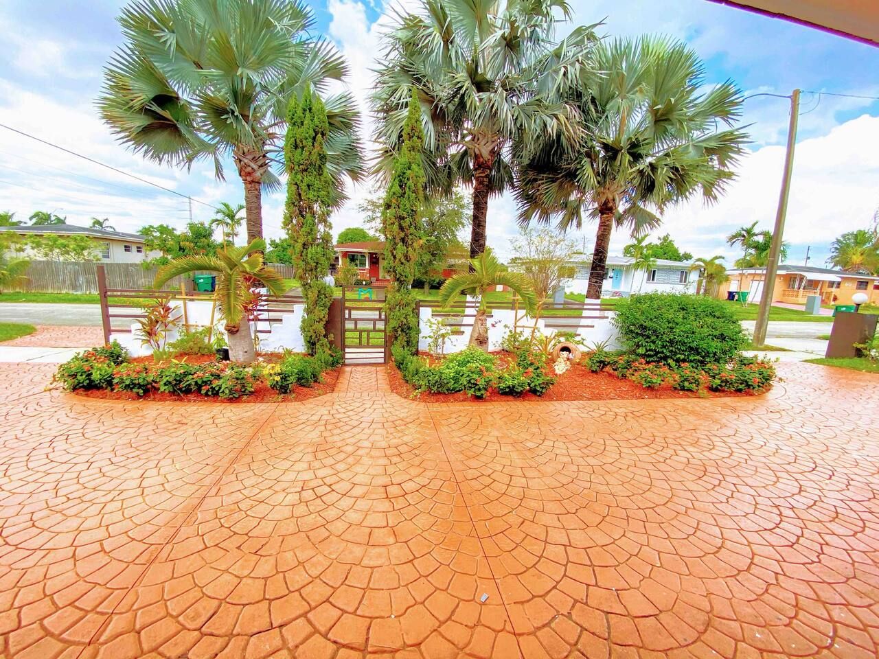 A paved entrance area with palm trees and a gate.