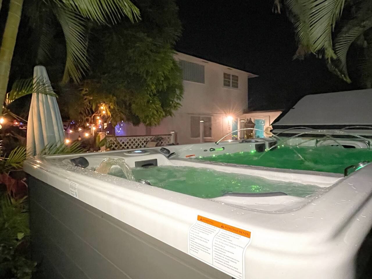 A hot tub with a label, surrounded by greenery and a building in the background.