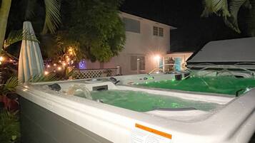A hot tub with a label, surrounded by greenery and a building in the background.