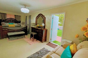 Un dormitorio con cama, cómoda, tocador y puerta que da a un balcón con vistas a la vegetación.