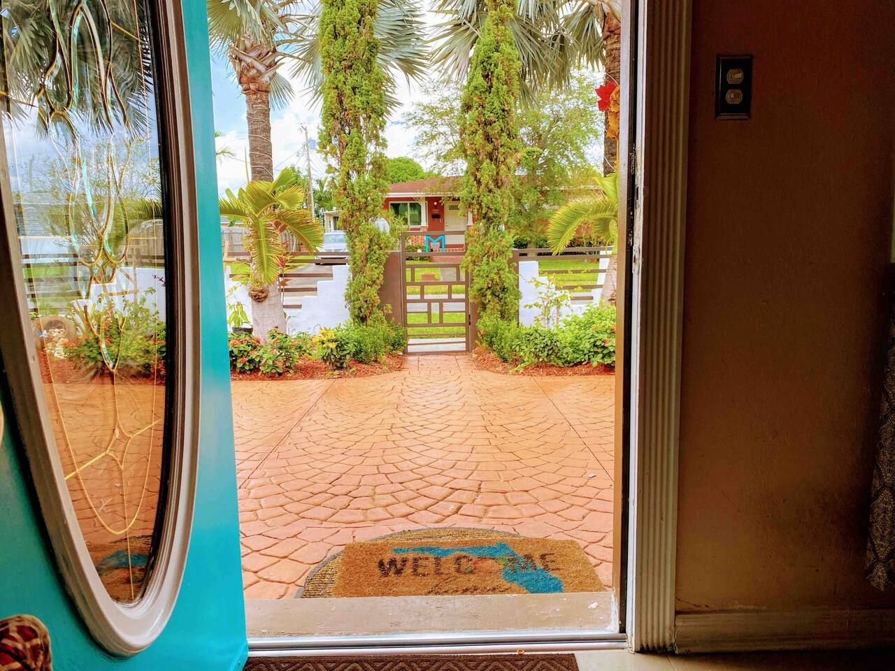 A doorway with a welcome mat and a view of a paved entrance leading to a building with a gate.
