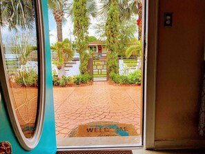 A doorway with a welcome mat and a view of a paved entrance leading to a building with a gate.
