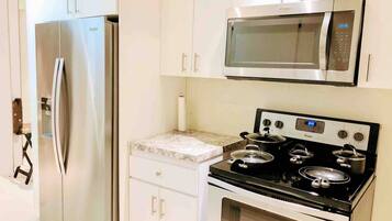 A kitchen with a stainless steel refrigerator, a microwave, and a stove with pots.