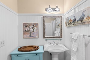 Un baño con tocador azul claro, un lavabo blanco, un espejo con marco decorativo y dos luces empotradas.