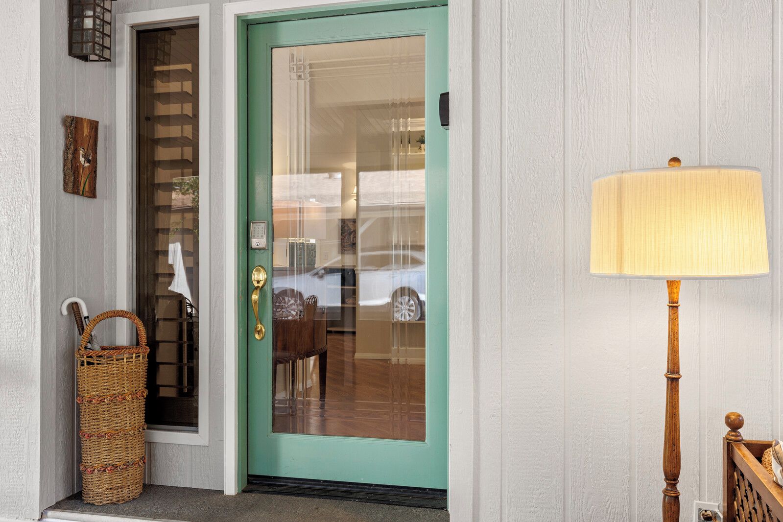 A teal door with a glass panel, a wicker basket, and a lamp on the right.