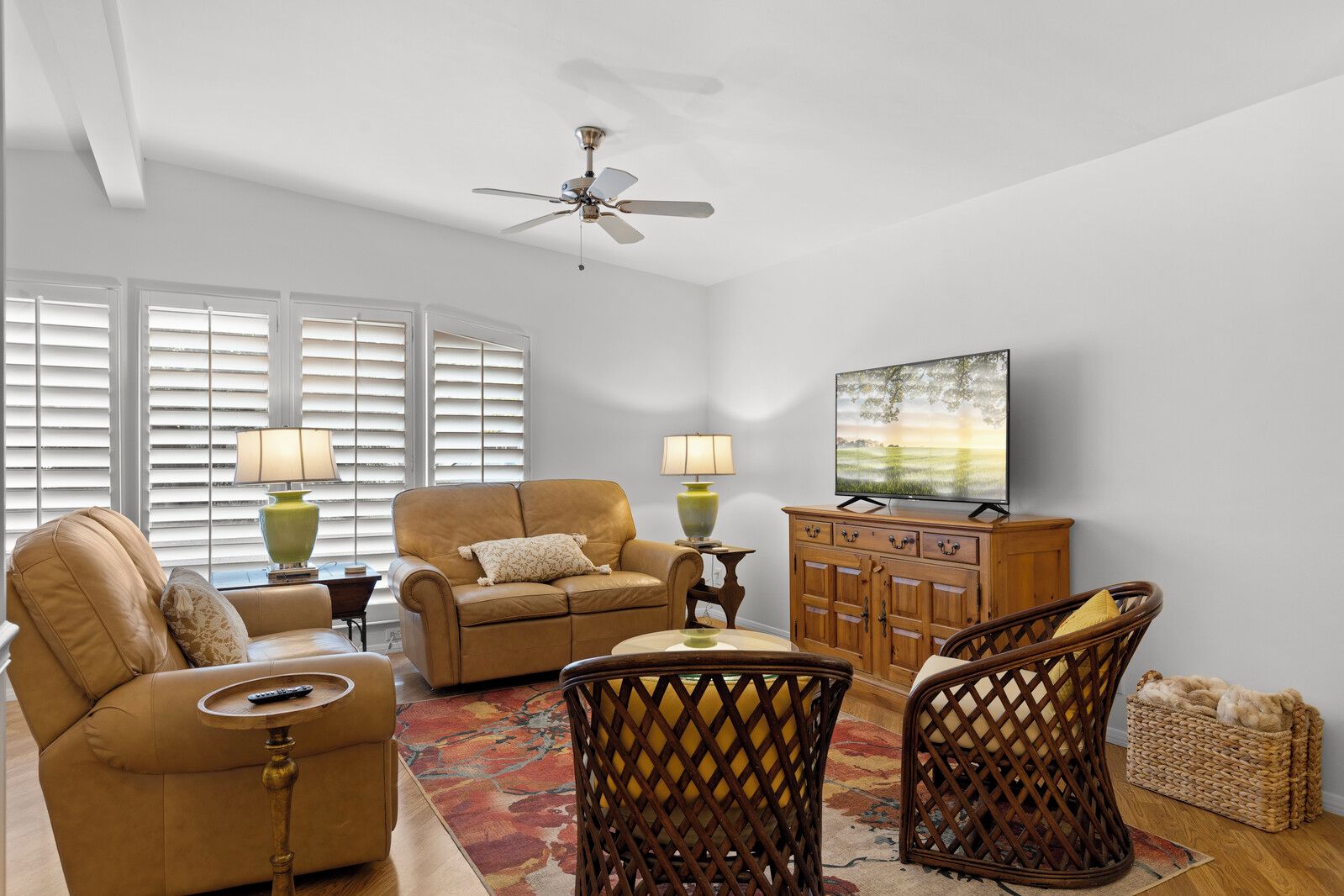 A living room with a sofa, armchairs, a coffee table, a television, and a ceiling fan.