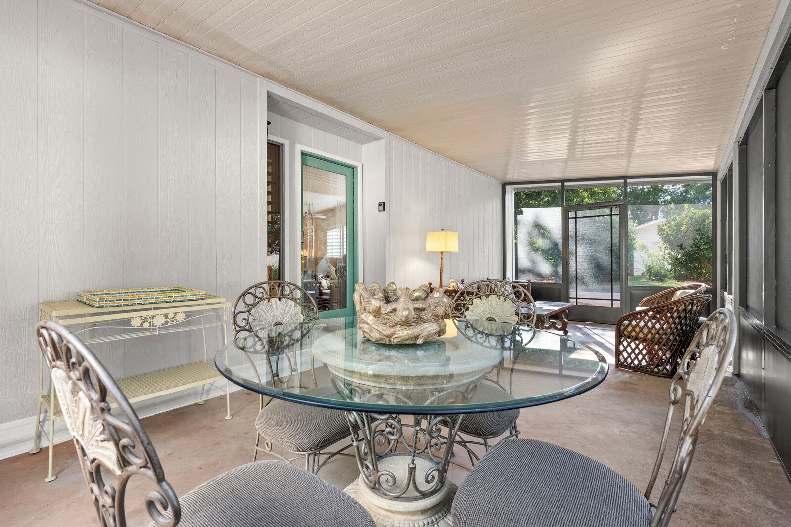 A dining area with a glass table surrounded by metal chairs, a cushioned bench, and a wicker basket.
