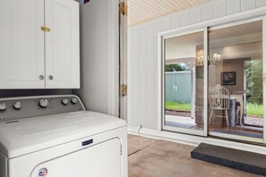 A laundry area with a white Maytag washer and dryer, a white cabinet, and a sliding glass door leading to an outdoor patio with a table and chairs. - Steps to Oak Creek – A Peaceful Sedona Retreat Near Cathedral Rock (Sedona)