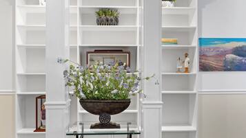 A room with white shelving units, a glass table with a decorative bowl, and a framed picture on the wall.