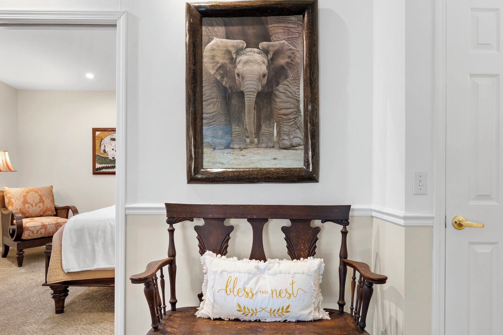 A bedroom with a wooden headboard, a framed elephant picture, and a bedside pillow with text.