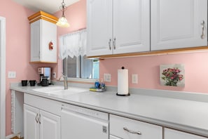 A kitchen with white cabinets, a stainless steel sink, a coffee maker, and a paper towel holder.