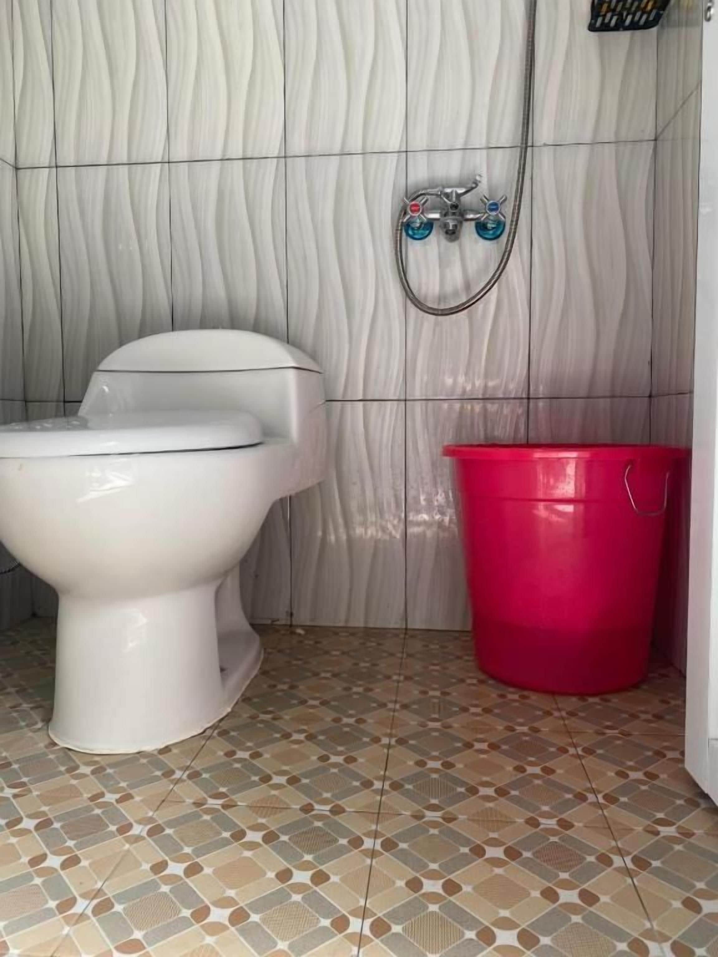 A bathroom with a toilet, a shower, and a red bucket.