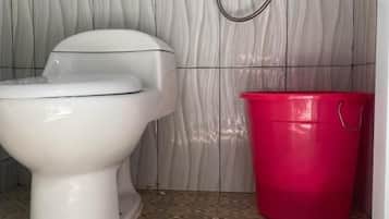 A bathroom with a toilet, a shower, and a red bucket.