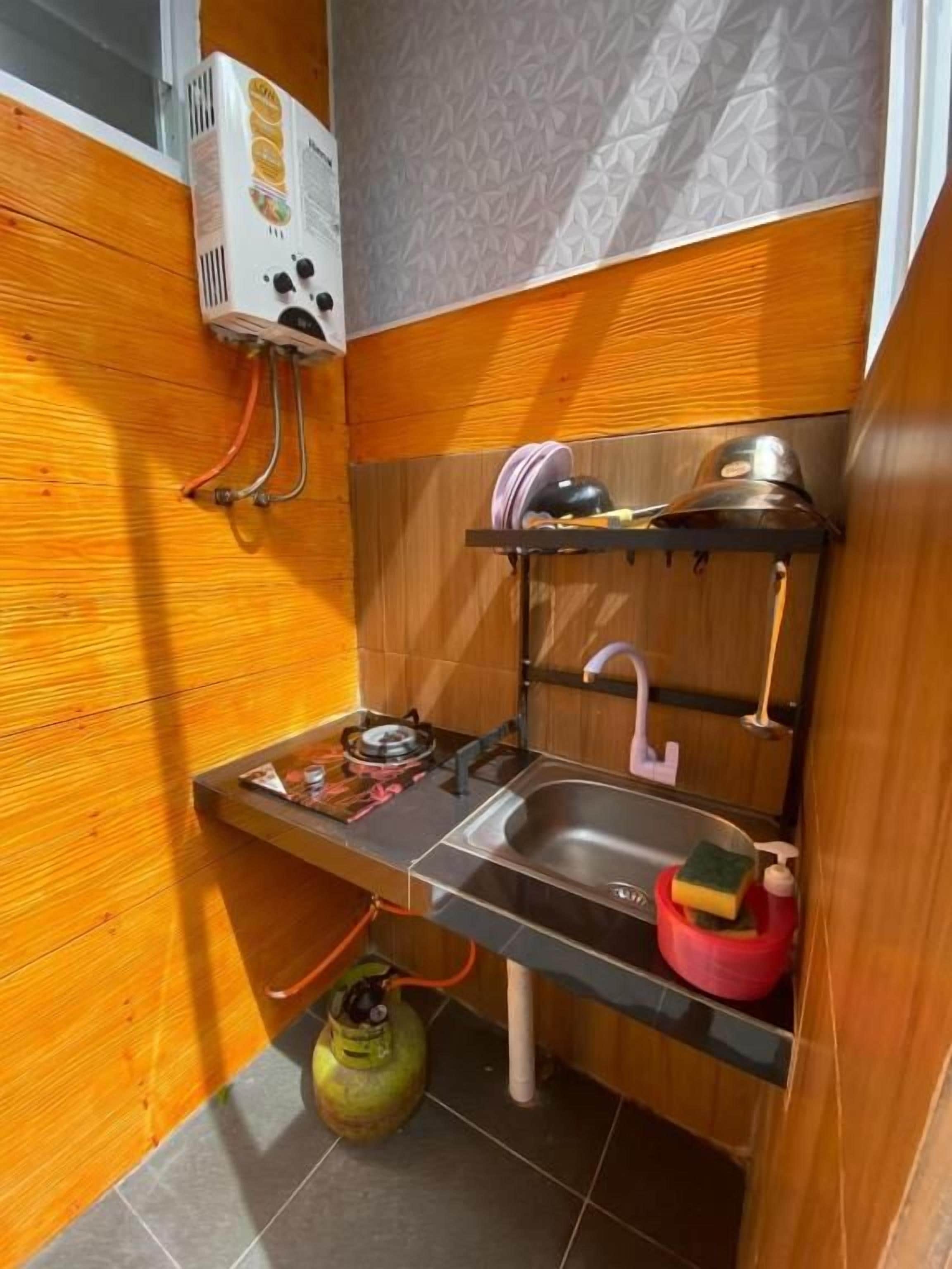 A compact kitchen with a gas stove, sink, and a gas cylinder.