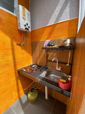 A compact kitchen with a gas stove, sink, and a gas cylinder.
