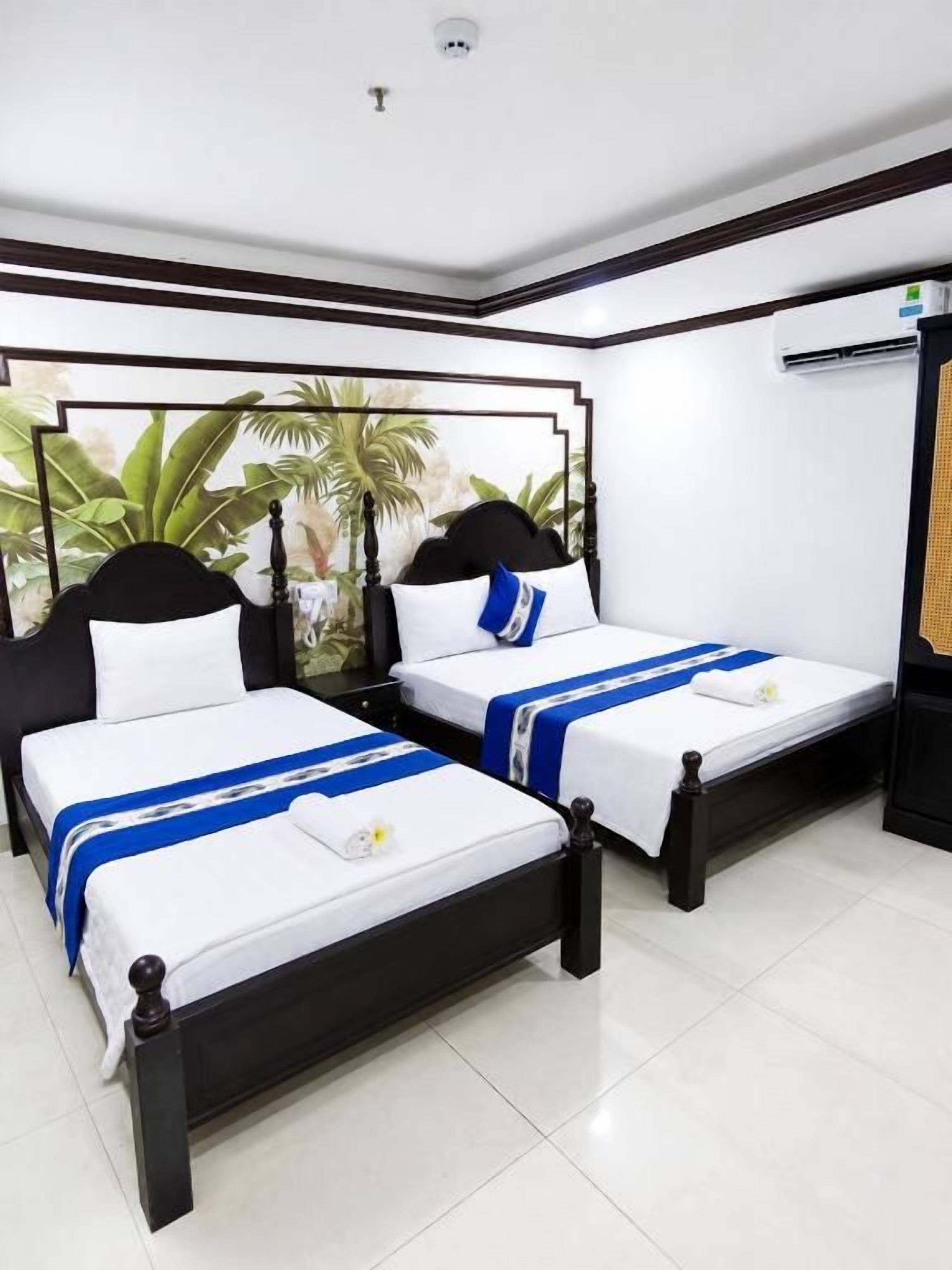 Habitación de hotel con dos camas, ropa de cama blanca y un mural temático tropical.