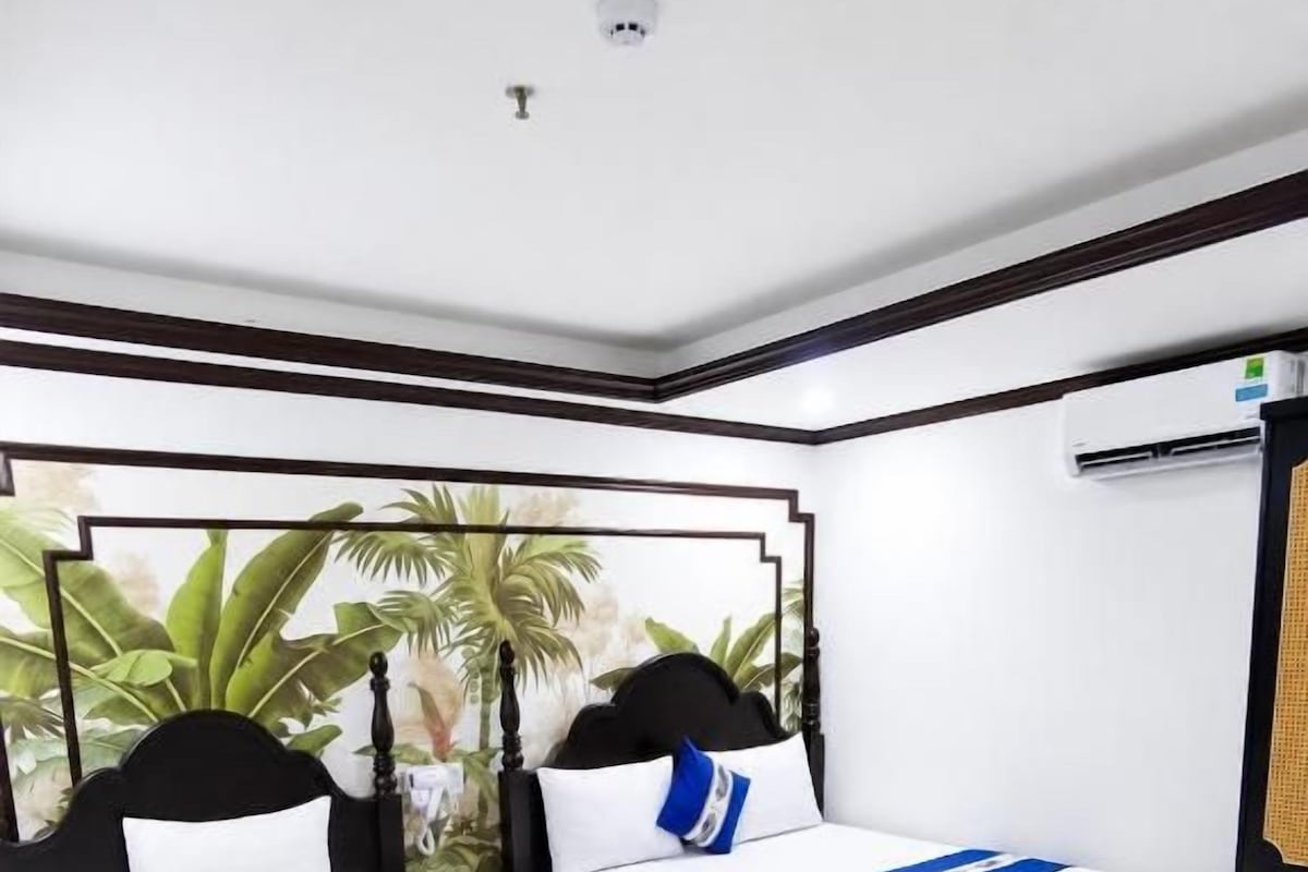 A hotel room with two single beds, a large window with a view of palm trees, and a ceiling-mounted air conditioning unit.