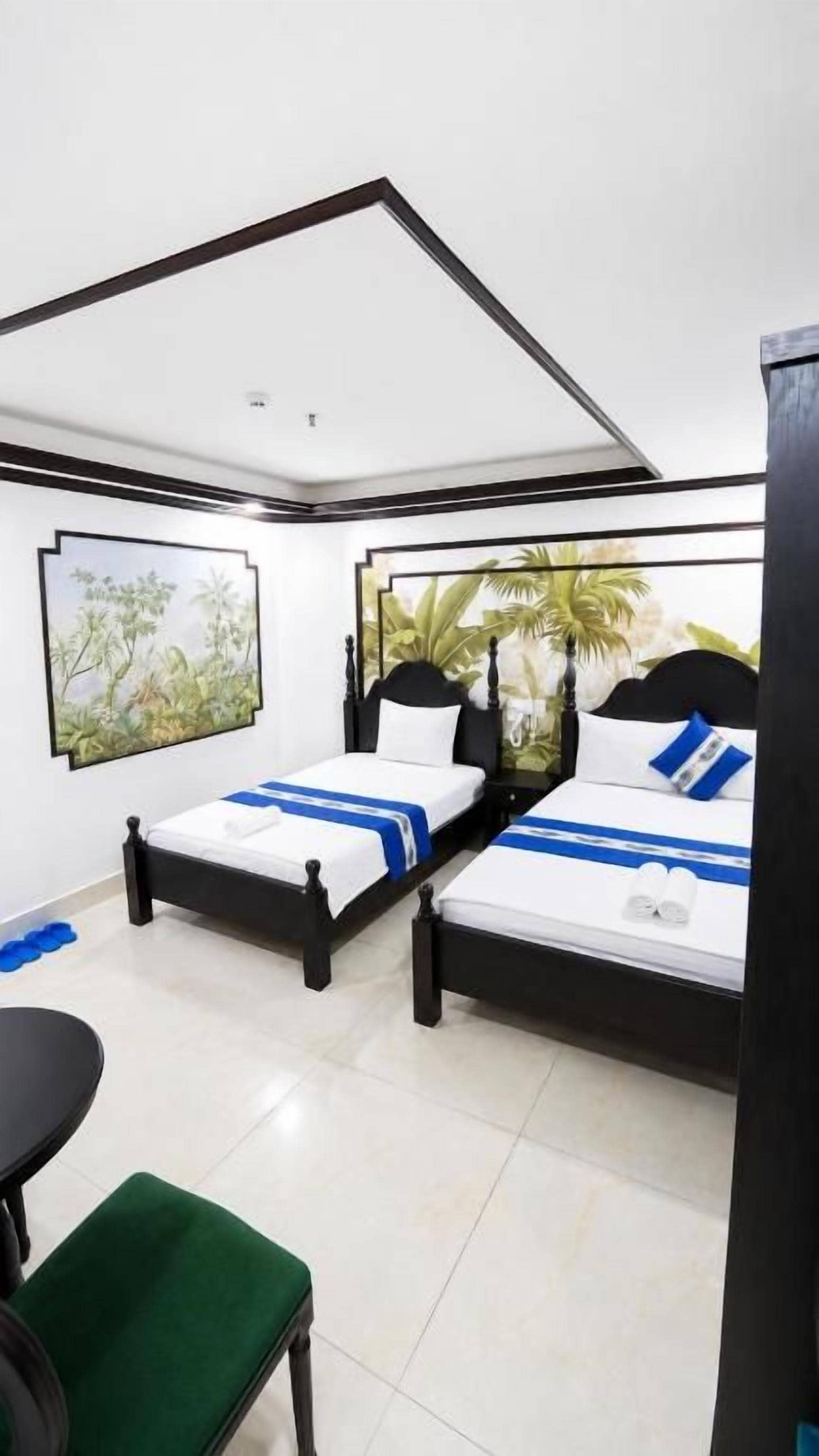 Habitación de hotel con dos camas, una silla verde y una mesita.