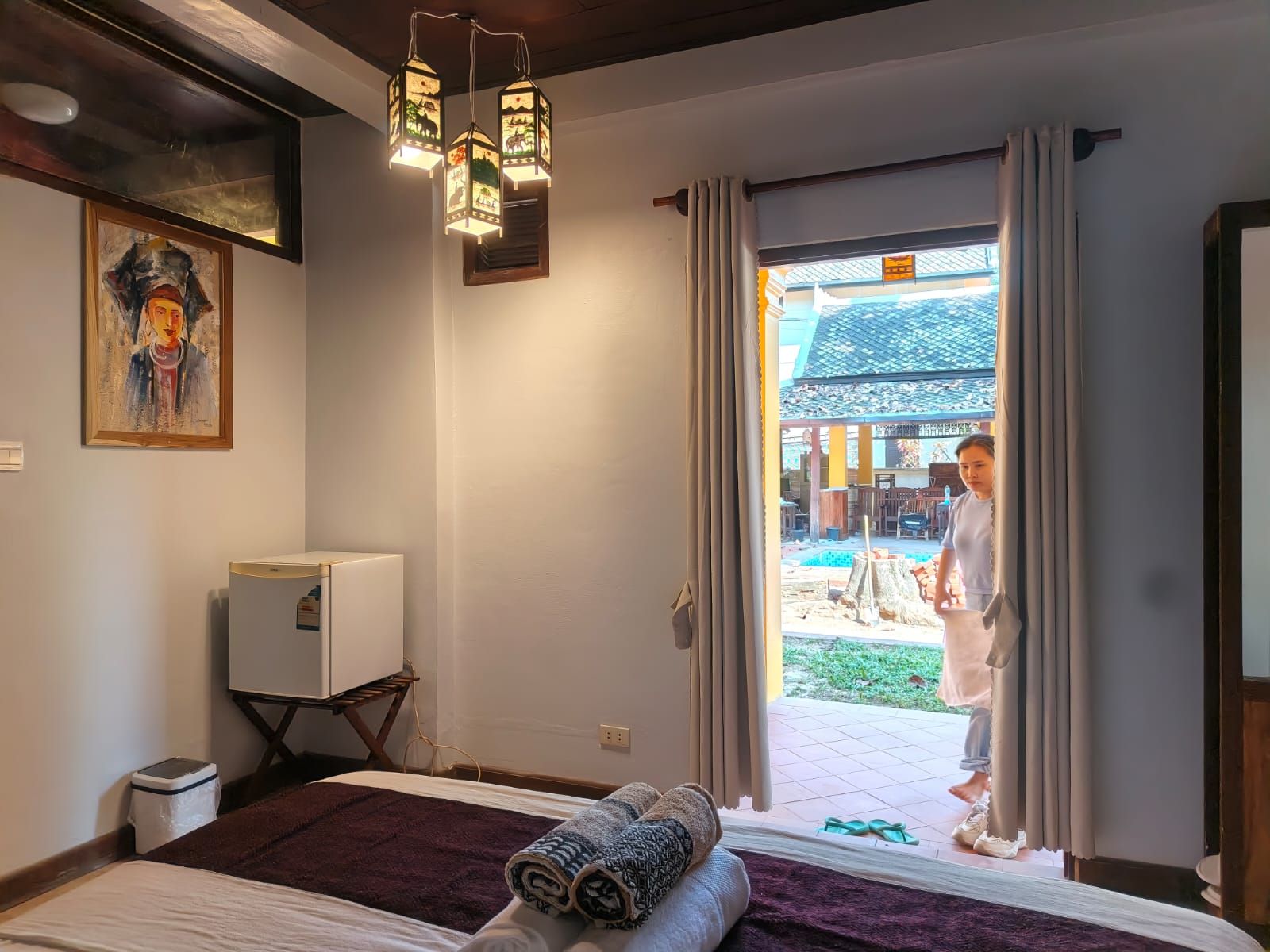Una camera d'albergo con un letto, una piccola televisione, un quadro e vista su uno spazio esterno con una persona.