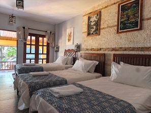 Ein Hotelzimmer mit drei Betten, einem Balkon und einer Backsteinwand mit Kunstwerken.
