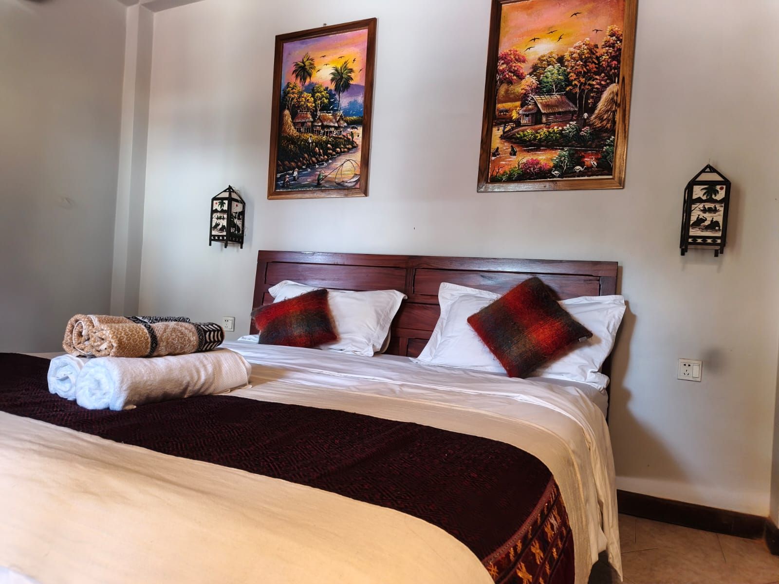 A hotel room with a large bed, two wall-mounted paintings, and a small decorative item on the wall.