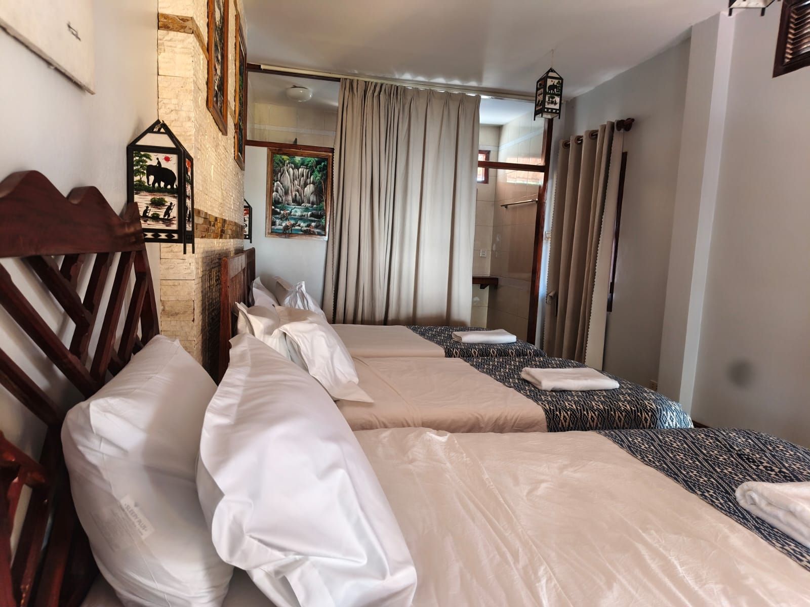 Une chambre d’hôtel avec deux lits, une tête de lit en bois, un tableau accroché au mur et une fenêtre avec des rideaux.