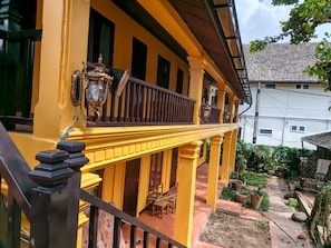 A yellow building with a balcony, a staircase, and a garden area with potted plants.
