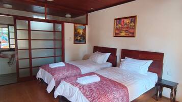 A room with two beds, a wooden ceiling, a wall-mounted painting, and a window with a view.
