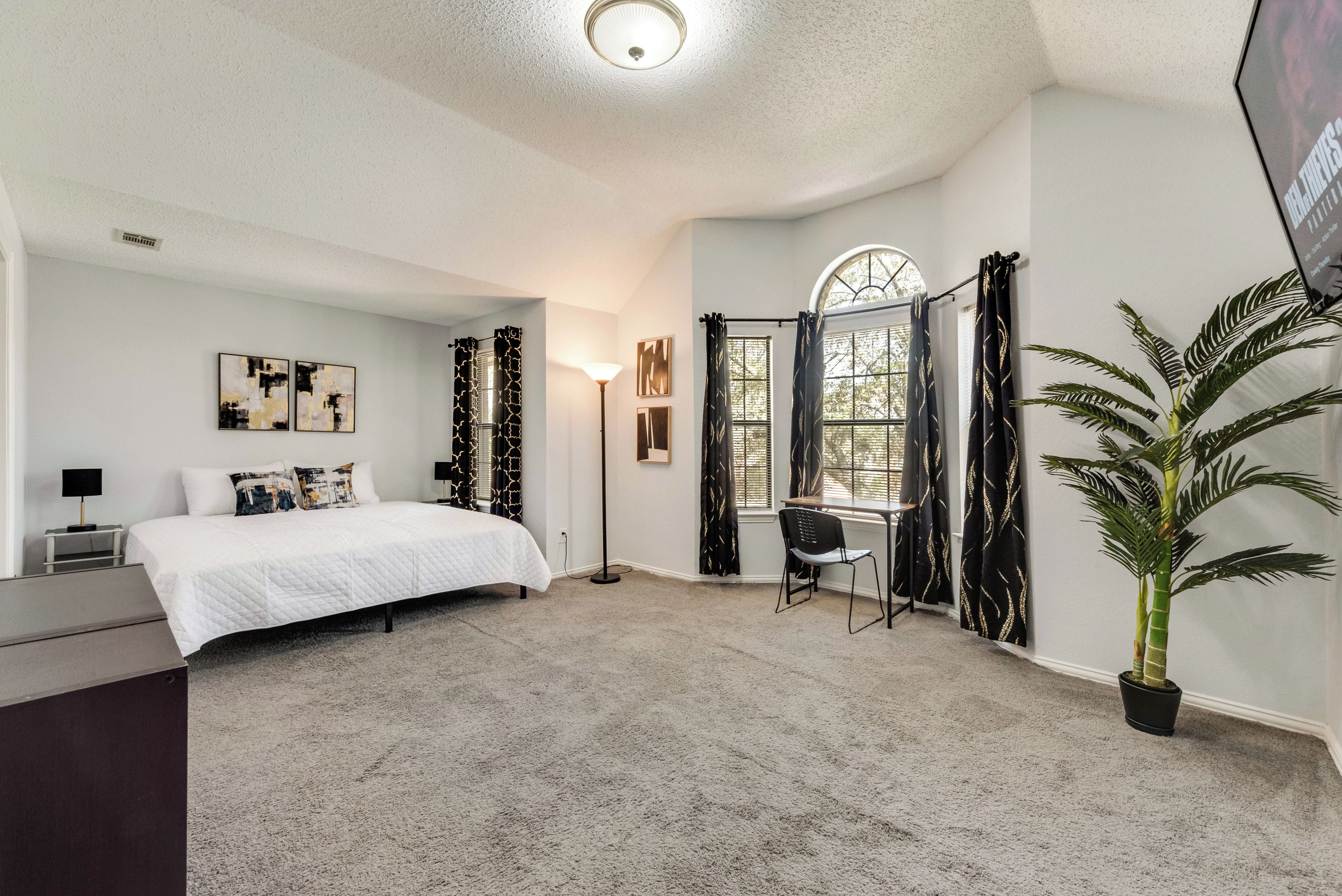 A bedroom with a bed, a desk, a chair, a potted plant, and a window with curtains.
