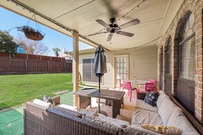 Une terrasse couverte, aménagée avec du mobilier d’extérieur et dotée d’un ventilateur de plafond, offrant une vue sur le jardin arrière.