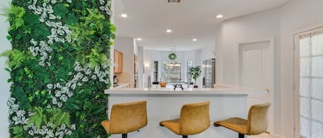 Una cocina moderna con barra, tres taburetes de bar y un jardín vertical verde.