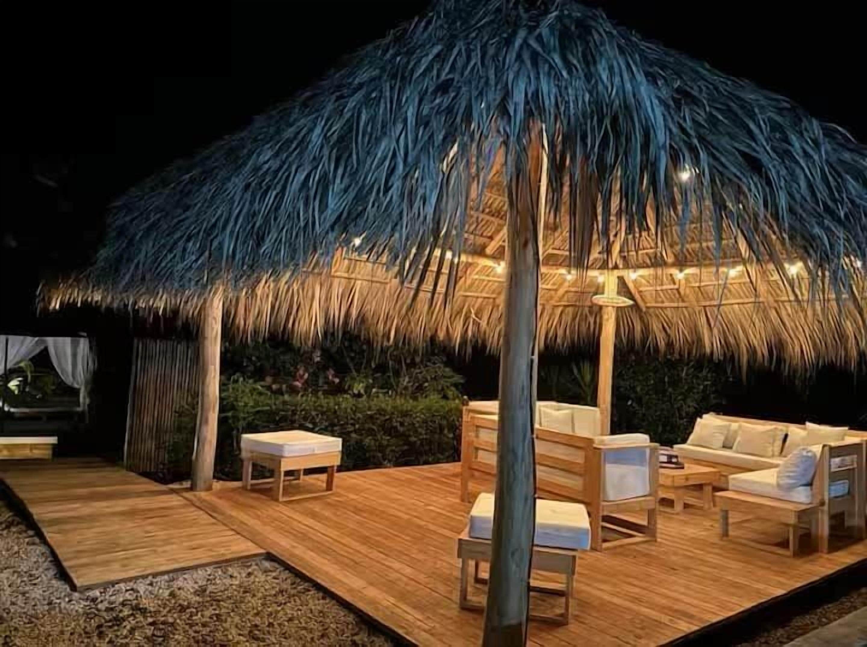 Un espace extérieur aménagé avec une structure à toit de chaume, un sol en bois et des sièges rembourrés.