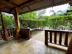 An outdoor covered area with a concrete floor, wooden railings, and a view of dense greenery. - Tropical Lodge The Hidden Hideaway (Playa Grande)