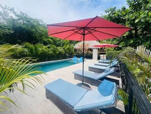 A pool area with lounge chairs and a red umbrella. - Tropical Lodge 
Hidden Hideaway-House (Playa Grande)