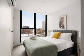 A modern hotel room with a large window, a bed with a grey headboard, a yellow pillow, and a painting on the wall. - Free Parking. Walk to Marvel Stadium & CBD (West Melbourne)