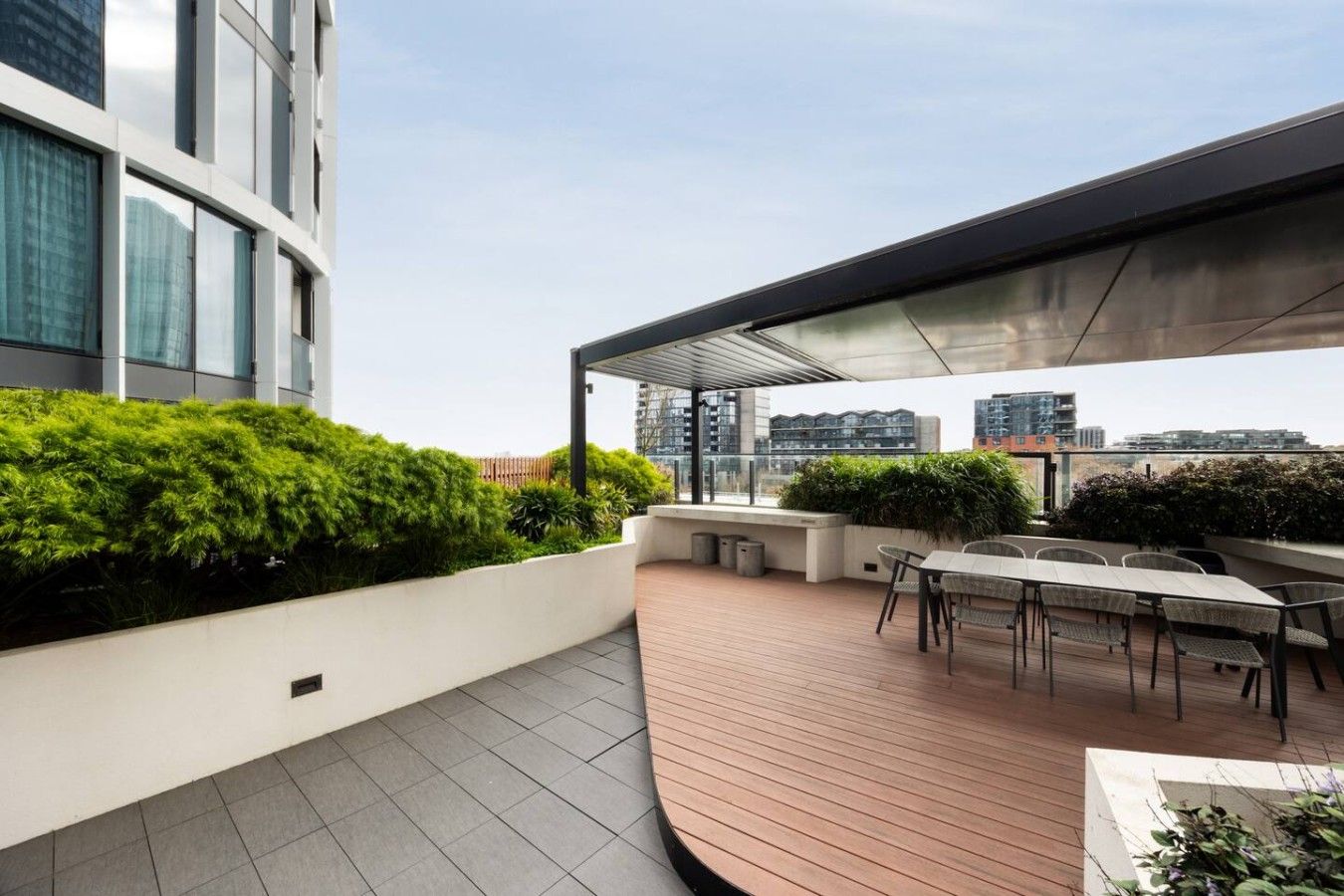 Una terraza en la azotea con zona de estar techada, una mesa y vistas al horizonte urbano.