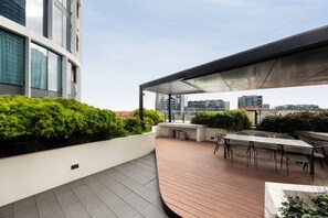 Terraço no telhado com área de estar coberta, uma mesa e vista para o horizonte da cidade.