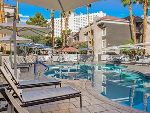 A hotel pool area with sun loungers, umbrellas, and a clear view of the surrounding buildings. - Club Wyndham Desert Rose Resort (Las Vegas)